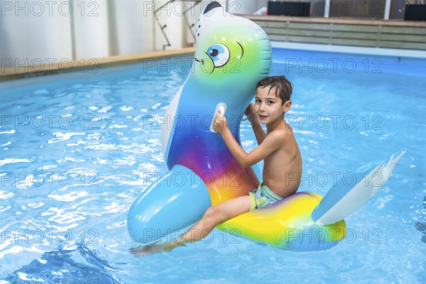 Boy enjoying summer holidays while riding an inflatable toy in a vibrant blue swimming pool, embracing the joy of childhood fun