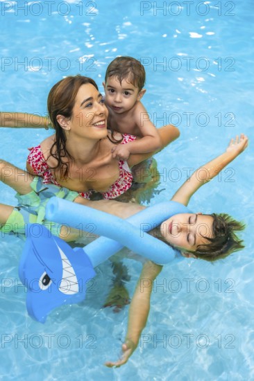 Mother and children enjoying summer vacation in a resort swimming pool, playing with inflatable toys and floating devices