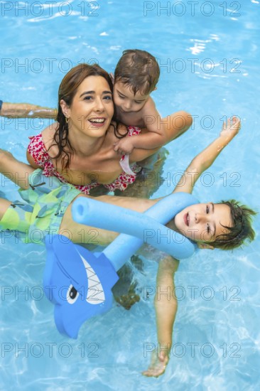 Happy family enjoying summer vacation, playing with inflatable toys in a refreshing blue swimming pool