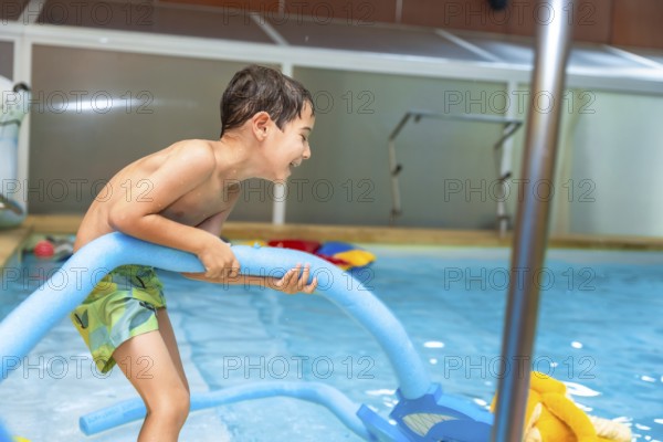Happy boy playing with a pool noodle in an indoor swimming pool, relishing a fun summer activity while enjoying the water and sunshine