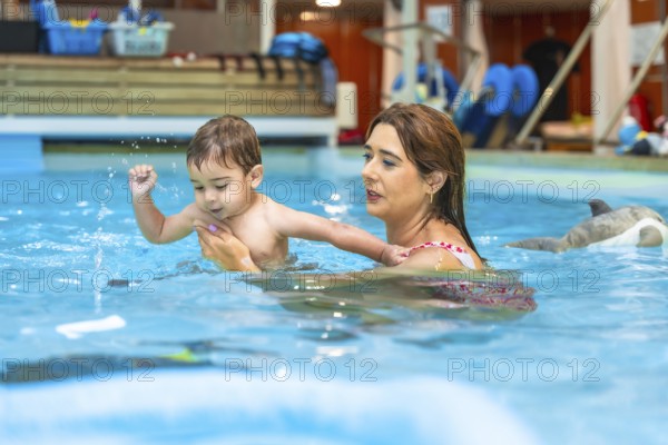 Swimming instructor holding baby swimming in indoor pool during a lesson, promoting water safety and early childhood development