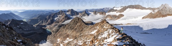 Mountaineer on a rocky ridge on the Wilder Freiger mountain peak, behind signal peak and Becher peak with Becherhaus, picturesque high mountain landscape, view of Übeltalferner glacier and rocky mountain peaks Königshofspitz and Sonklarspitze, Stubai Alps, South Tyrol, Italy