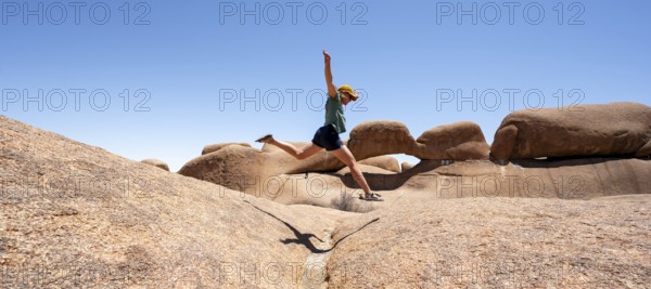 Tourist jumping over rocks, rock formation, Pontok Mountains, Spitzkoppe, Great Spitzkuppe Nature Reserve, Namibia