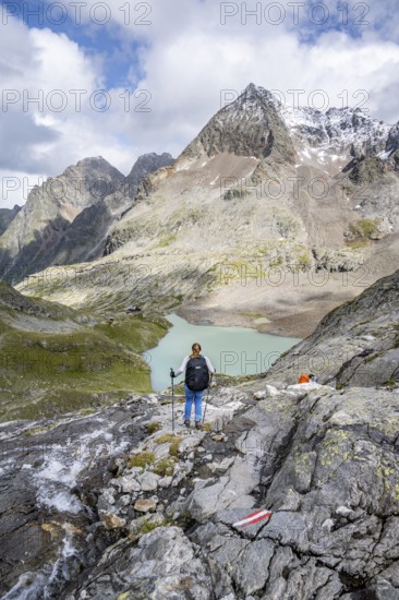 Mountaineer on a rocky hiking trail, view of the turquoise-blue mountain lake Großer Gradensee, behind her the summit of the Petzeck, Hoher Perschitzkopf and Kruckelkopf, Schober Group, Hohe Tauern National Park, Carinthia, Austria
