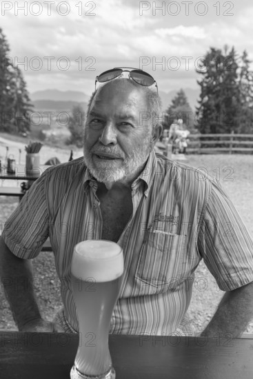 Elderly gentleman with beard and sunglasses in a garden restaurant with a drink, black and white, Bavaria, Germany