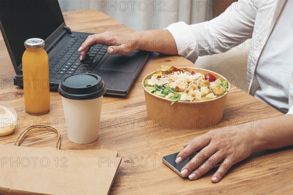 A woman is working on a laptop at home, there is food on the table, salad, coffee and juice, delivery, work at home