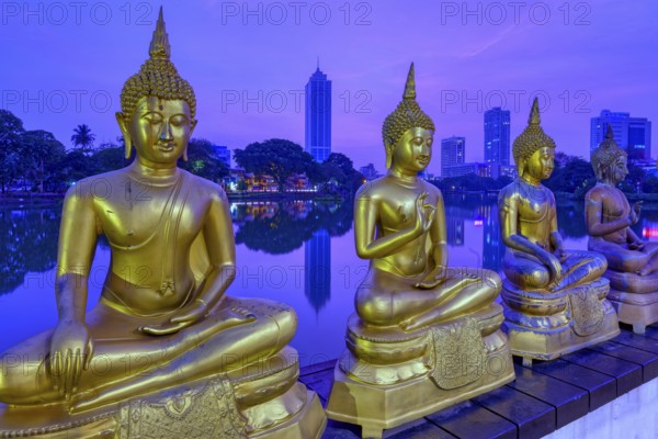 Buddha statues of Seema Malaka Temple at Beira Lake at sunset, Colombo skyline behind, Sri Lanka