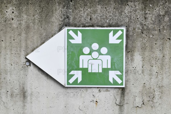Emergency assembly point sign on concrete wall. Indicates designated safe meeting area for evacuation or disaster situations