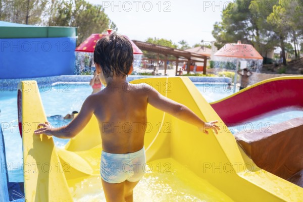 Young boy climbing up a vibrant yellow waterslide at a lively water park, embracing the joy of summer fun and adventure
