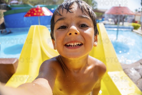 Smiling boy taking a selfie while having fun on a waterslide at a water park during summer vacation