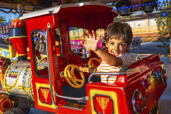 Smiling child enjoying a ride on a vibrant amusement park train, waving enthusiastically. Bright colors and playful atmosphere enhance the fun experience