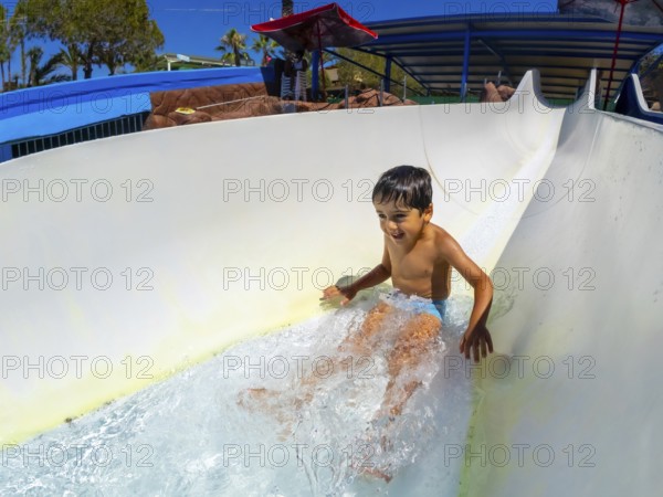 Excited boy sliding down a waterslide at an amusement park, reveling in the joy of summer vacation and the thrill of adventure