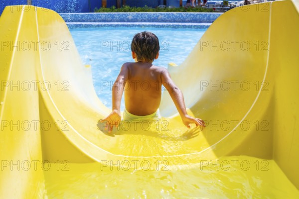 Boy joyfully sliding down a colorful waterslide in an aquapark, enjoying summer vacation with laughter and excitement under the sunny sky