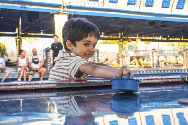 Smiling boy playing air hockey at an amusement park, surrounded by colorful lights and people, capturing the joy of childhood fun
