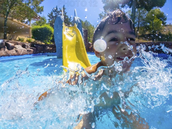 Young boy having fun going down a water slide and splashing into a refreshing pool on a sunny summer day