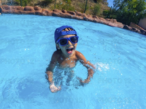 Young boy enjoying summer vacation, playing in a refreshing blue pool, wearing a cap and sunglasses