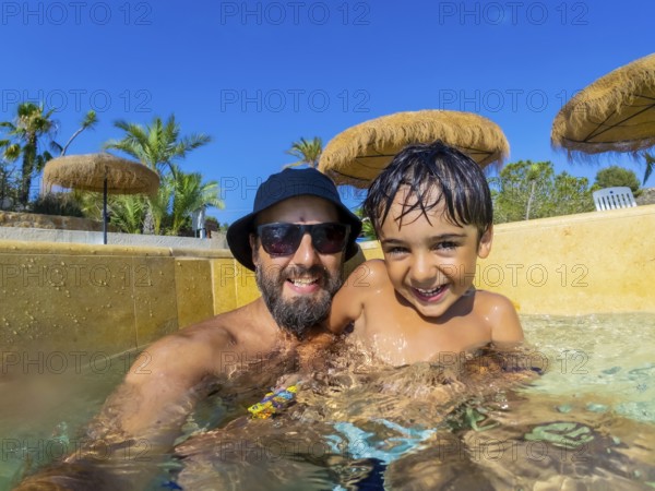 Happy father and son are spending quality time together, playing in swimming pool during summer vacation
