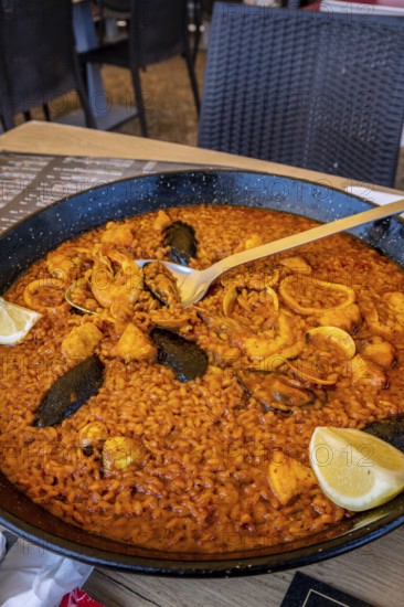 Steaming paella with mussels, shrimp, and calamari, served in a traditional pan and garnished with lemon, ready to be enjoyed