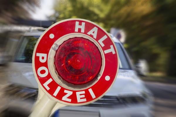 (Photomontage) Symbolic image of a police check: close-up of a police trowel labelled HALT POLIZEI in front of a car