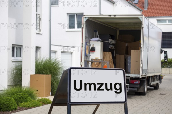 (Photomontage) Relocation symbolic image: lorry in front of a residential building, in front of it a stand with the inscription UMZUG