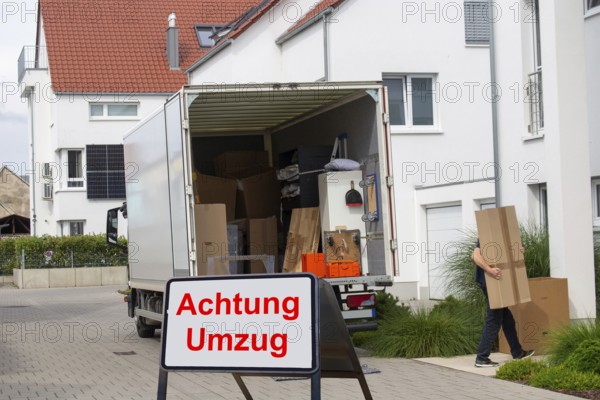 (Photomontage) Relocation Symbolic image: lorry in front of a residential building, in front of it a sign with the inscription ATTENTION RELOCATION