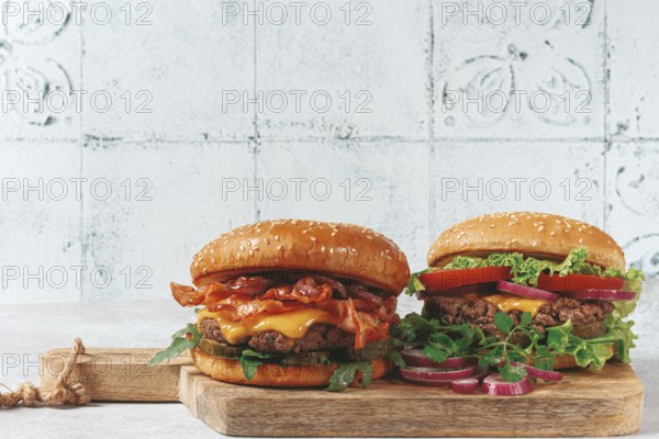 Two burgers with beef patty, fried bacon, cheddar cheese, tomatoes, on a light table
