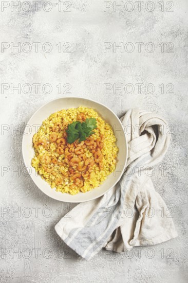 Risotto with shrimp, in a bowl, on a textured surface, with a side dish of fresh coriander, homemade, no people