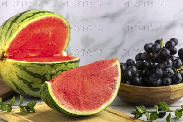 Sliced watermelon and grapes on a wooden board with mint leaves