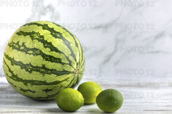 Watermelon and limes on a wooden surface against a marbled background