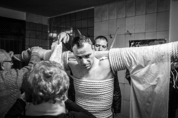 A man is tied to a cross with hemp ropes, carrying two swords in his back and a shroud over them, preparing for the procession of the Empalaos, every Maundy Thursday in Holy Week, Valverde de la Vera, Extremadura, Spain