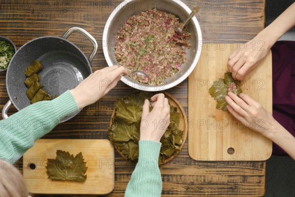Hands skillfully roll seasoned meat mixture into grape leaves, surrounded by pots and cutting boards. The cozy kitchen is filled with the aroma of spices, highlighting the art of making dolma