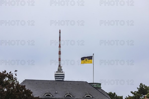 State flag of Baden-Württemberg on the Villa Reitzenstein, official residence of the Minister President. Behind it the top of the Fernseturm. Stuttgart, Baden-Württemberg, Germany