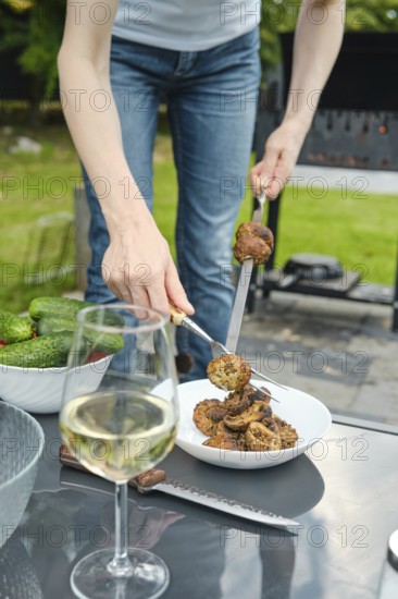 Unrecognizable woman put grilled champignons in a plate with a fork