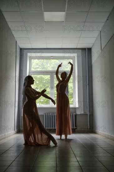 Silhouette of two ballerinas in transparent dress rehearsing choreography in the hallway of theatre