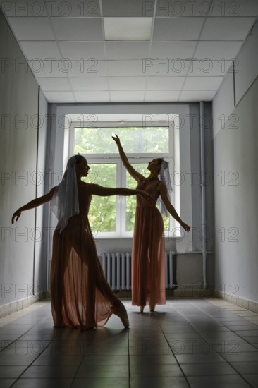 Silhouette of two dancers performing graceful artistic moves with their hands in corridor of theatre