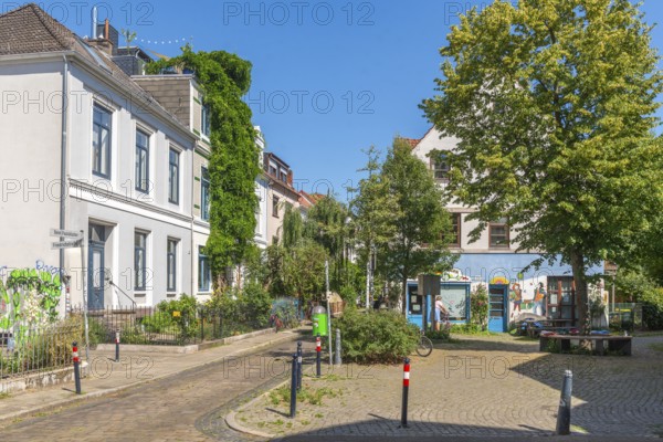 Residential street in the Ostertor neighbourhood a popular residential area, eastern suburb, Wilhelminian style buildings, traffic-calmed, graffiti, square with tree and bench, green facades, cobblestones, sunshine, Bremen, Germany