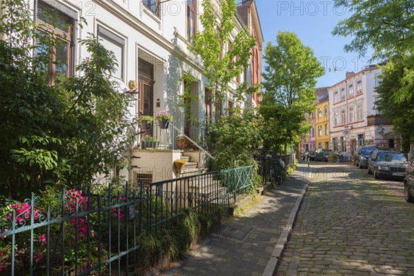 Residential street in the Ostertor neighbourhood a popular residential area, eastern suburb, Wilhelminian style building, stairs to the entrance, facades, cars parked, small front garden, plants and trees, metal fence, cobblestones, traffic-calmed, Bremen, Germany