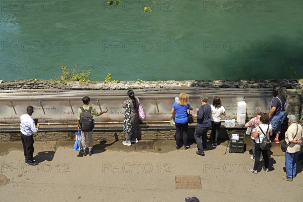 Pilgrims at the fountain with the holy water from the spring of the Marian pilgrimage site of Lourdes, Pyrenees, France