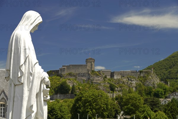 Statue on Rosary Square and the ChÃ¢teau fort de Lourdes fortress in the Marian pilgrimage town of Lourdes, Pyrenees, France
