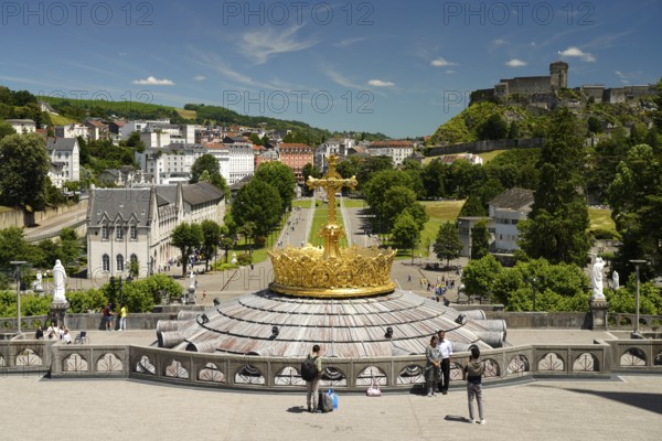 The gilded crown of the Basilica of the Rosary, Rosary Square and ChÃ¢teau fort de Lourdes fortress in the Marian pilgrimage town of Lourdes, Pyrenees, France