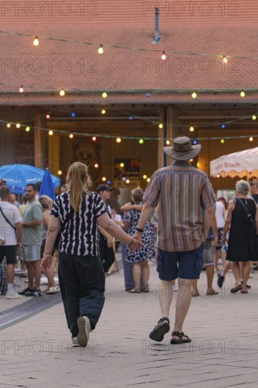 A couple holding hands and walking through a lively evening event, 950 years Weil der Stadt ceremony, Böblingen district, Germany