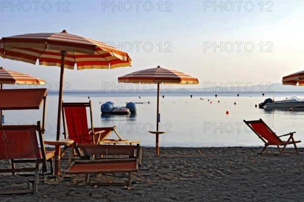 Beach, deckchairs, sunshades at the lido, Lake Bolsena, Lago di Bolsena, volcanic crater lake, calm smooth water surface, warm evening light, Bolsena, Province of Viterbo, Lazio, Italy