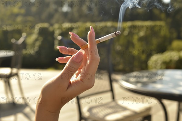 Elegant female hand with long pink nails holding a burning cigarette. Summer sunlight in outdoor cafe setting evokes style and contradiction. Generative ai, AI generated