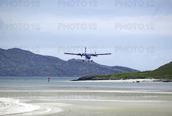 An aeroplane lands on a runway on the beach with mountains in the background and a calm atmosphere, Outer Hebrides, Isle of Barra, Scotland, United Kingdom