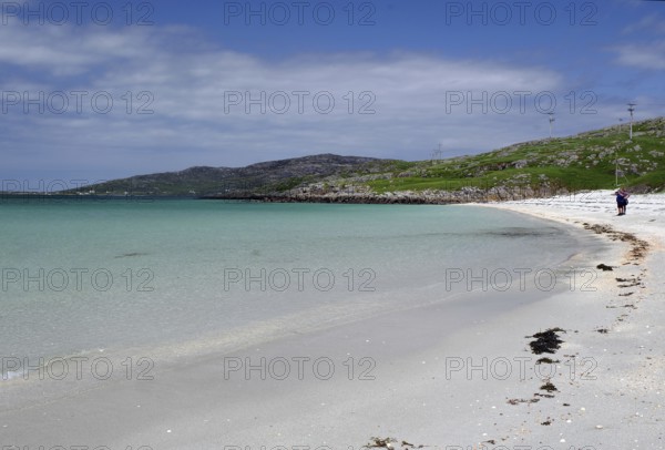 Clear bright blue beach with gentle waves under a cloudless sky, two people at the water's edge, Outer Hebrides, Eriksay, Scotland, United Kingdom