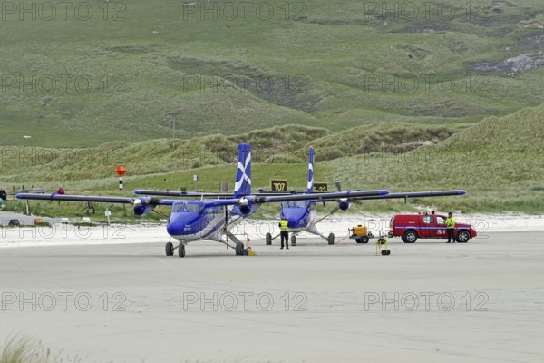 Aeroplanes standing on a runway in front of green hills, accompanied by a red vehicle, Outer Hebrides, Isle of Barra, Scotland, United Kingdom
