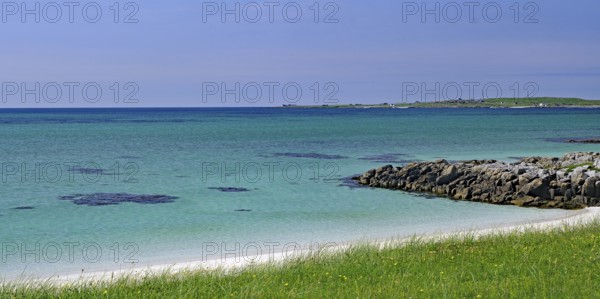 Clear blue sky over a rocky coastline with green grass and blue water, Outer Hebrides, South Uist, Scotland, United Kingdom