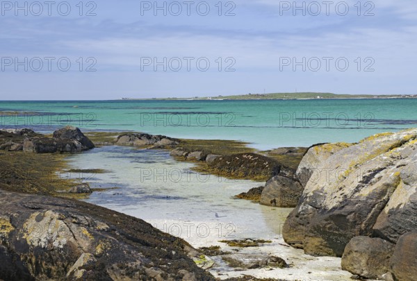 Rocky coastline with turquoise sea and gentle waves under a blue sky, Eriksay, South Uist, Scotland, United Kingdom