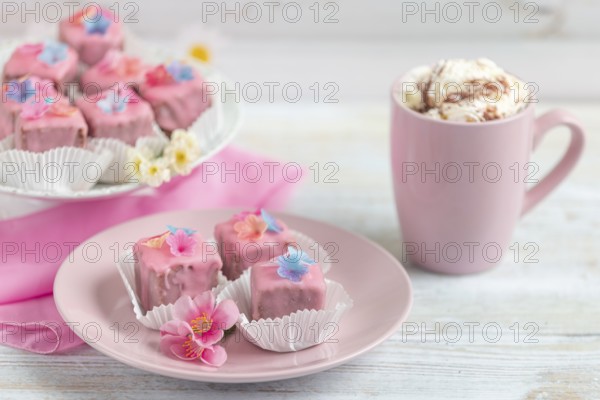 Pink petit fours and a cup of coffee with cream on a table