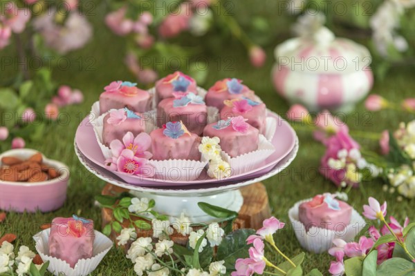 Pink petit fours with flower decorations on a plate in a colourful, floral setting